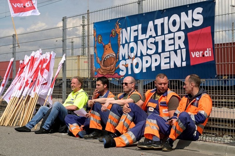 2022年6月9日在德国汉堡港口，工人们坐在写着“阻止通货膨胀怪物”的横幅前，要求提高工资。（图片来源：路透社）